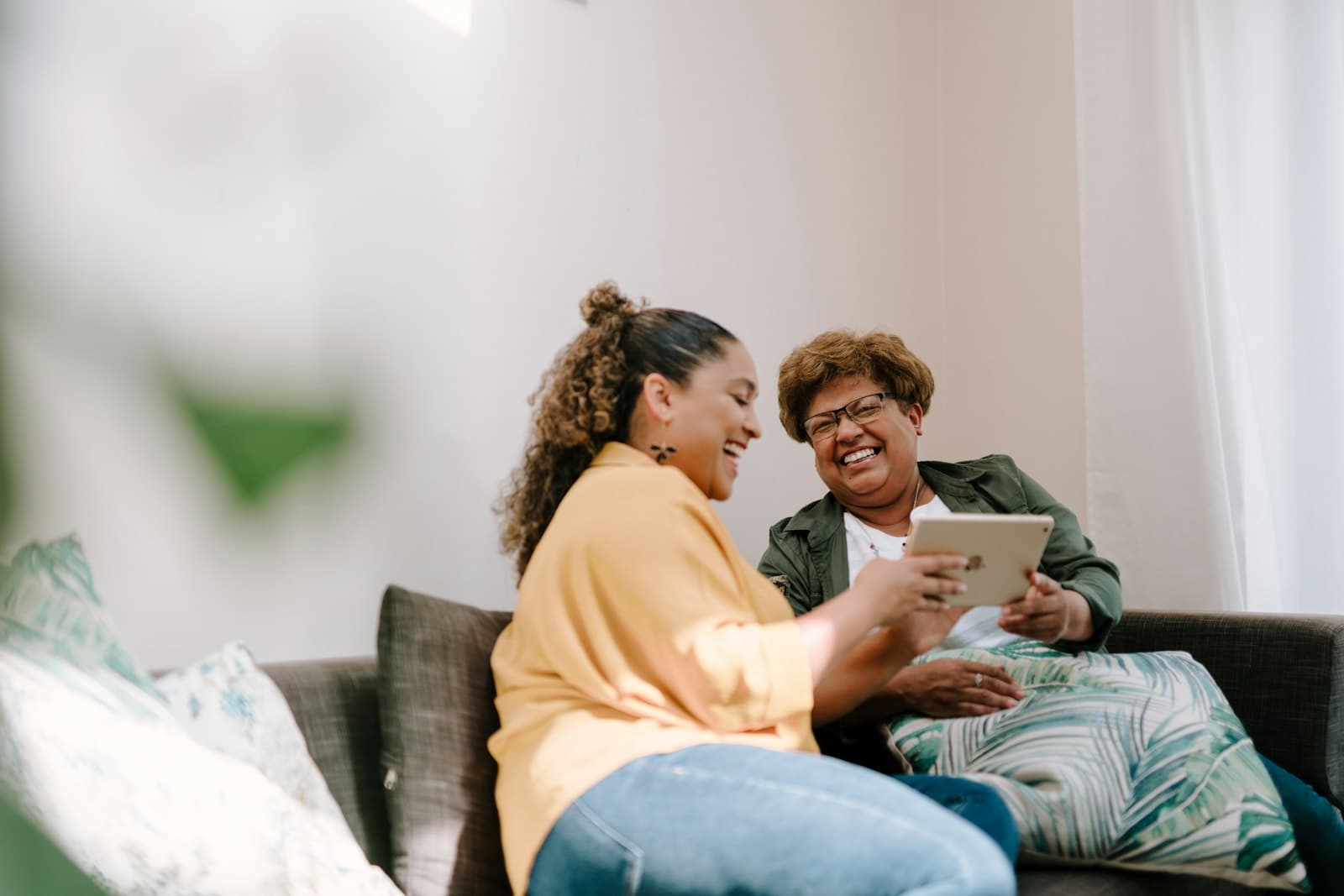 A caregiver and an older woman laughing together while looking at a tablet